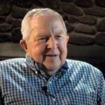 photo of man with white hair and blue patterned dress shirt smiling