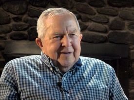 photo of man with white hair and blue patterned dress shirt smiling